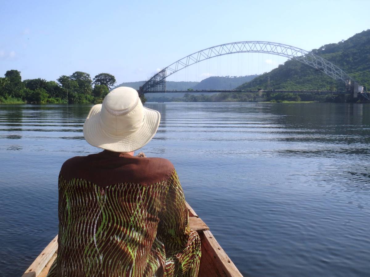 Guest in dugout canoe approaching the Adomi Bridge crossing the Volta River